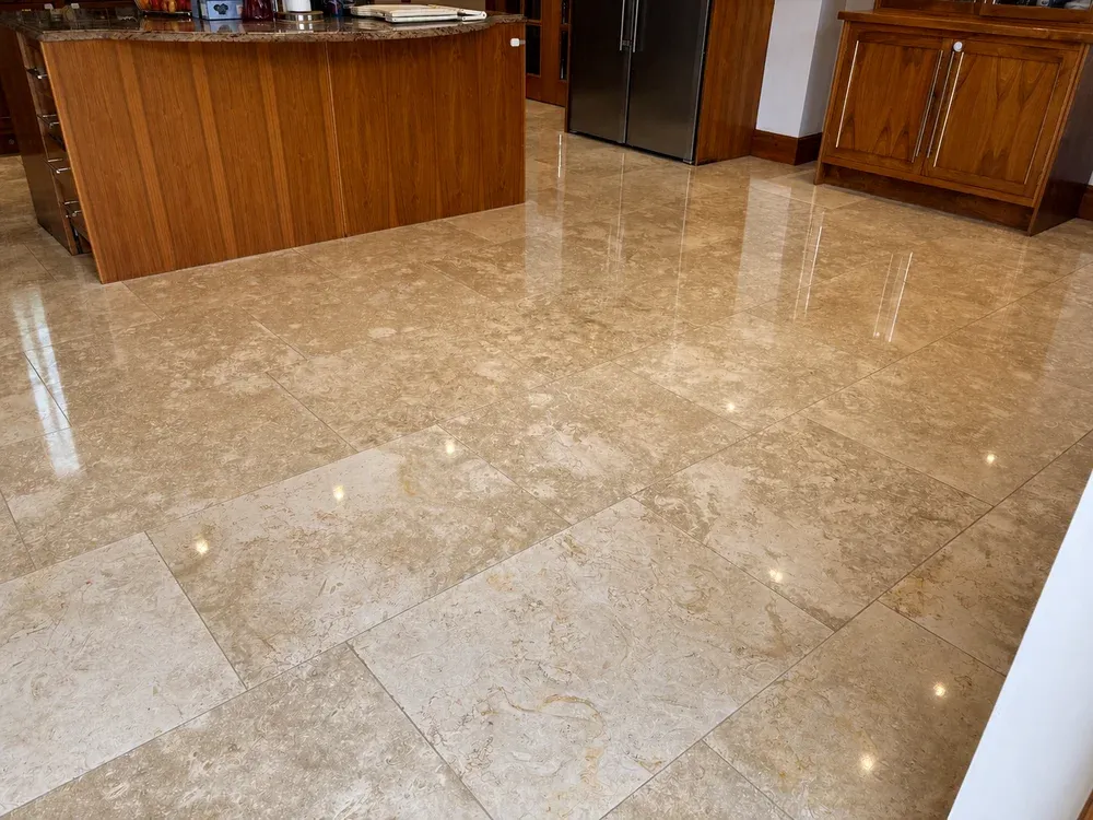 Mirror-polished travertine floor in a kitchen with a wood-panelled island and stainless steel fridge freezer.