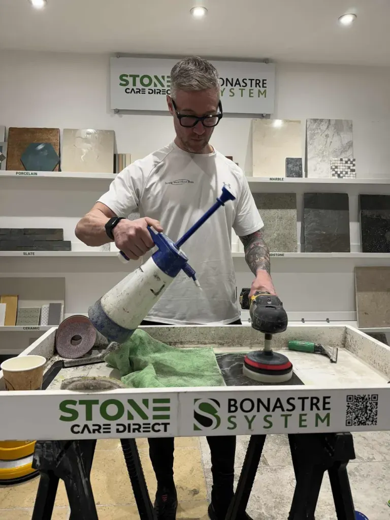 South West Floor Care technician polishing a small stone sample on a test rig, surrounded by marble and slate tile samples.