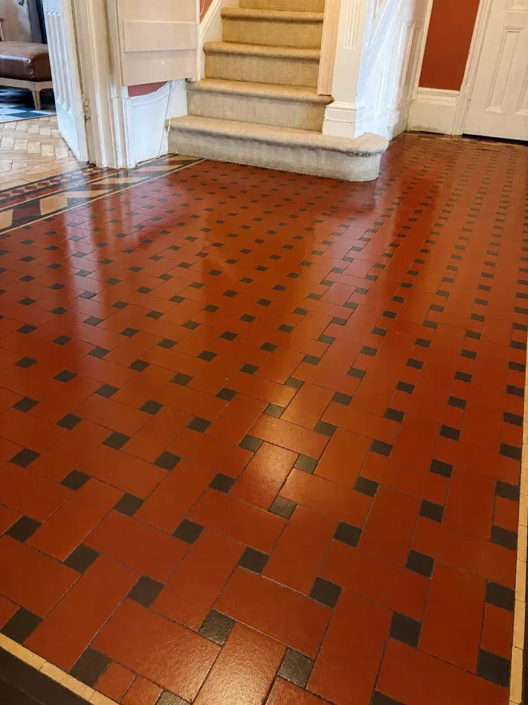 Polished red and black Victorian quarry tile hallway floor in a basket-weave pattern, leading to a carpeted staircase.